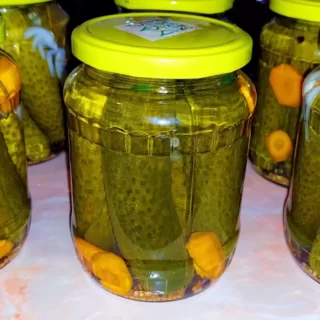 Glass Jars Filled with Green Dill Pickles, Tightly Sealed Placed Against a Neutral Background.